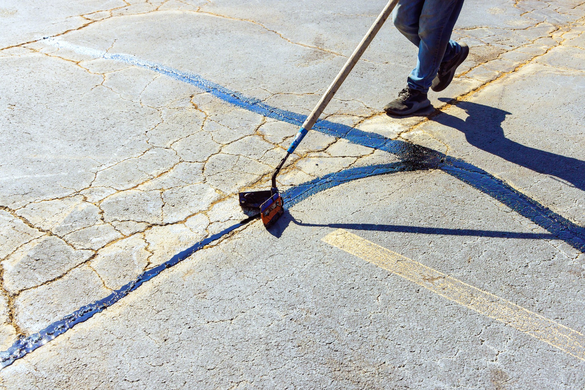 Worker patches asphalt cracks, seals them using bitumen emulsion, restores road